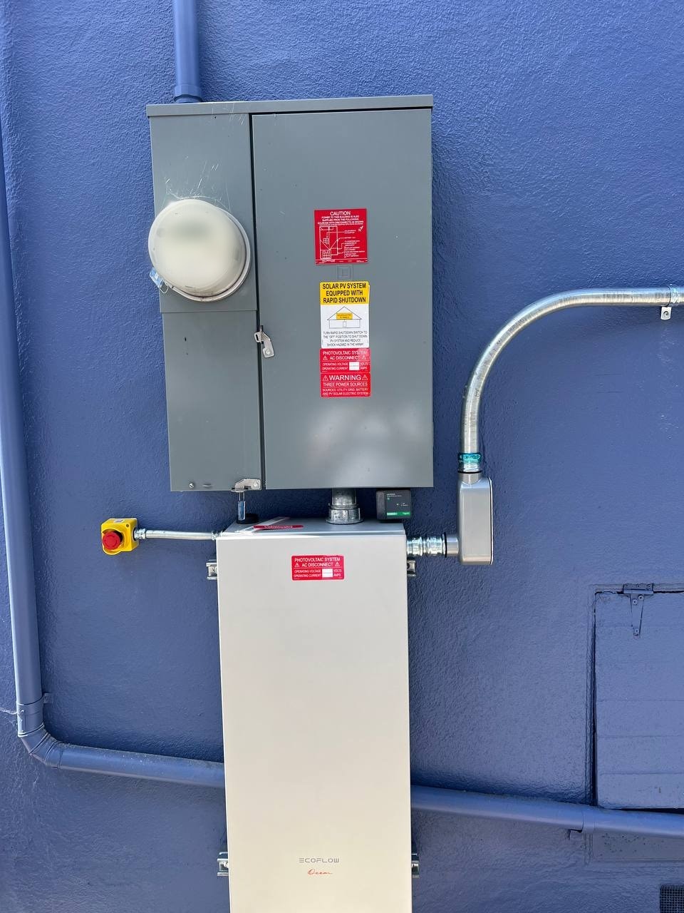 Rapid shutdown labeling and emergency shutoff hardware mounted on a blue wall, showing solar PV system disconnect equipment and NEC 690.12 required labels